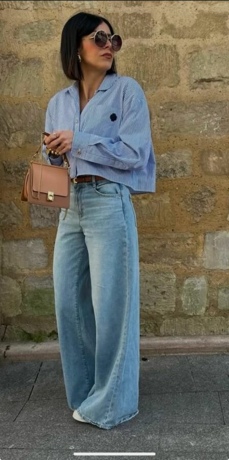 Woman wearing baggy light-wash jeans, striped cropped shirt, and carrying a tan handbag
