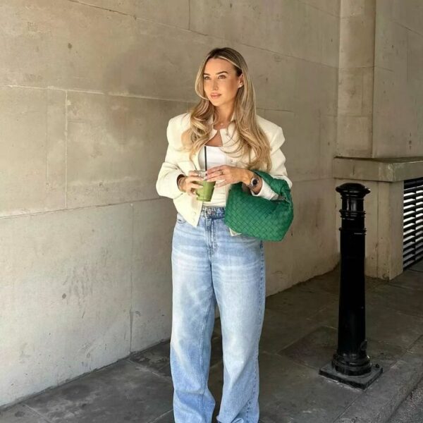 Woman wearing light-wash baggy jeans with a cream jacket, white top, and green handbag