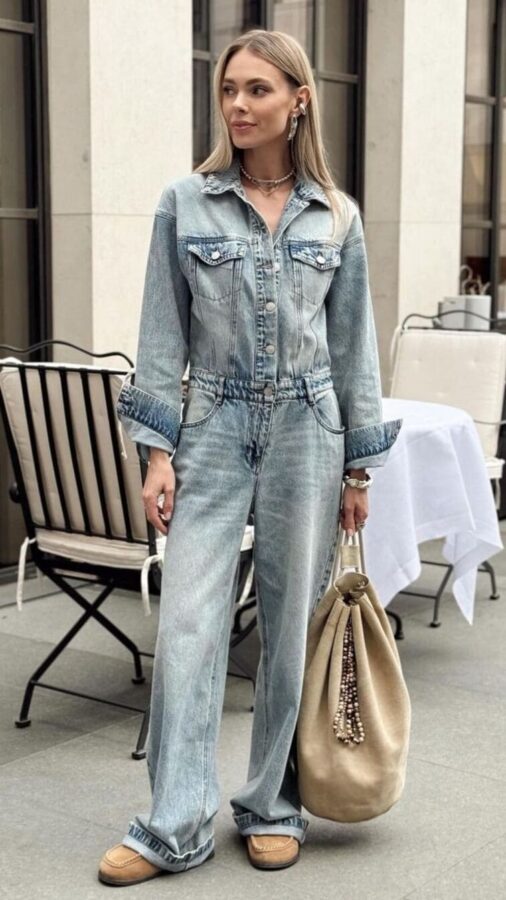 Woman in a tailored denim jumpsuit with rolled cuffs, moccasin-inspired shoes, and a bucket bag. 