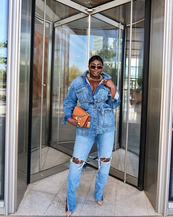 woman in jeans with a belt and worn jeans, accented by a handbag in orange and layered jewelry.