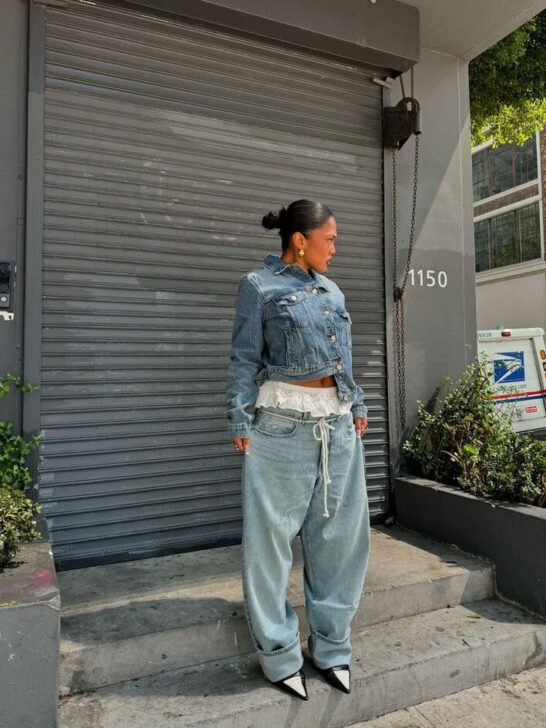 Woman wearing a cropped denim jacket with oversized jeans and black pointed heels.