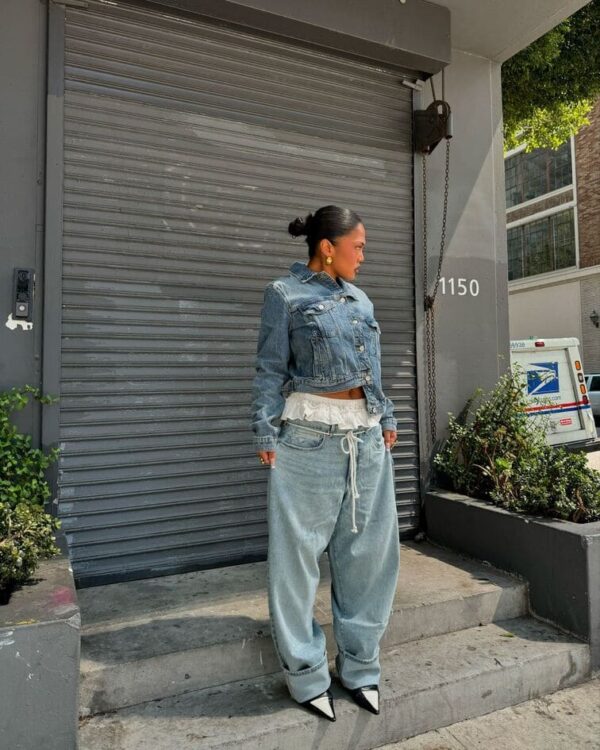 Woman wearing a cropped denim jacket with oversized jeans and black pointed heels.