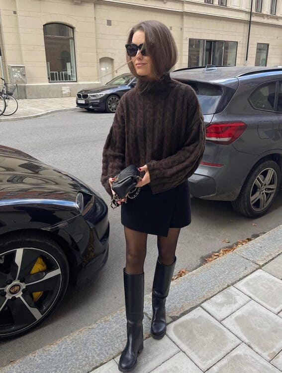 Cozy fall look with a mini skirt, oversized sweater, knee-high boots, and black handbag.