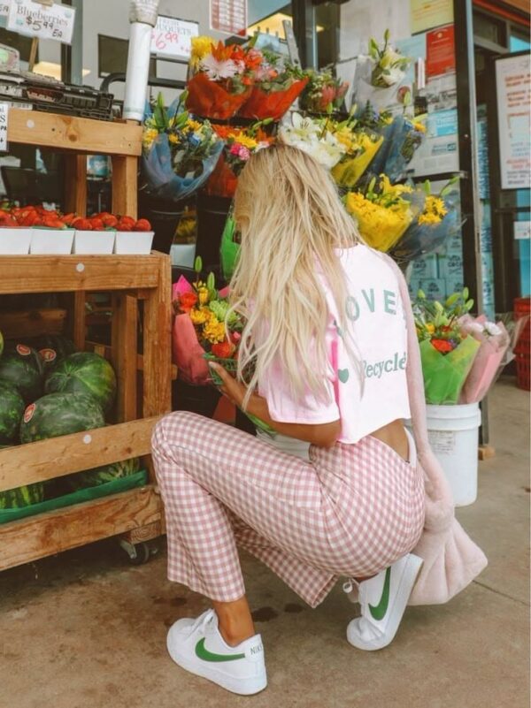 Woman at a flower market wearing a cropped graphic tee, pink gingham pants, and white Nike sneakers with a green swoosh