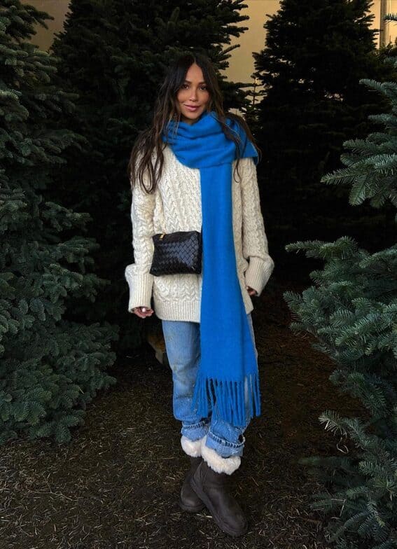 A woman wears an ivory sweater, blue jeans, and a vibrant cobalt scarf to complete a cozy winter ensemble.