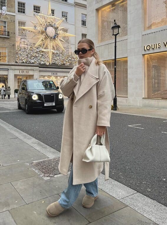 A woman in an off-white wool jacket, a turtleneck sweater, and blue jeans to create a chic winter outfit.