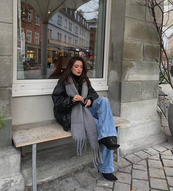 A woman is wearing black leather, a gray scarf, and light-washed jeans for an easy winter look.