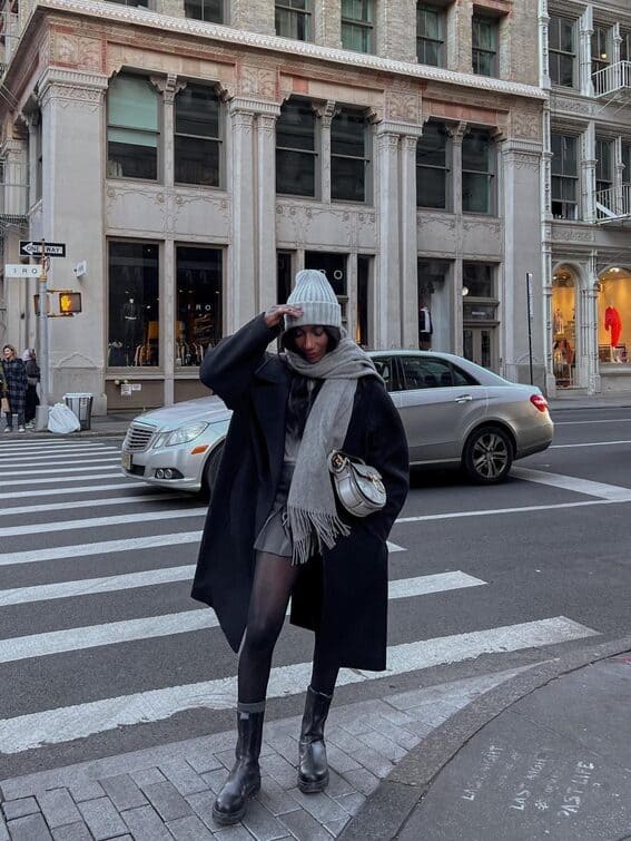 The woman is wearing an extra-large wool coat layered with a sweater, a mini skirt, and black tights for the perfect winter outfit.