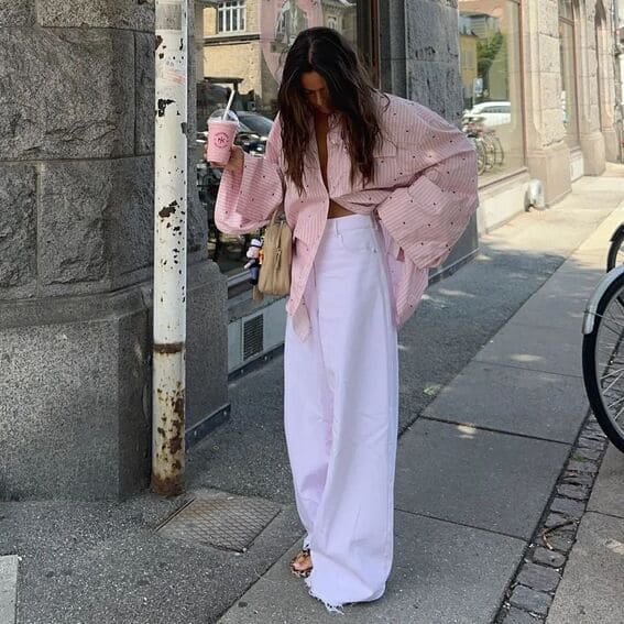 Casual and elegant outfit with an oversized pink striped shirt and loose white pants paired with a pair of sandals.