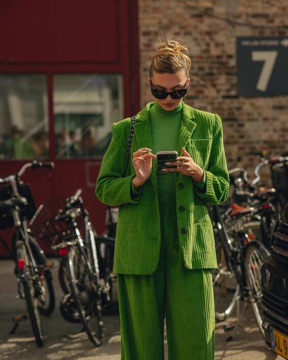 A striking green suit made of corduroy with a turtleneck that matches, coupled with dark shades.