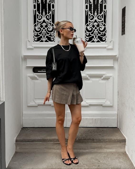 A stylish black oversized t-shirt paired with a pleated checkered mini skirt and sandals with strappy straps.