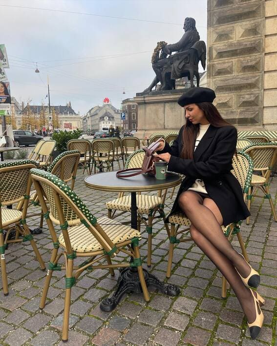 A fashionable woman in a cafe with a beret, a black blazer, and heels paired with the most revealing tights.