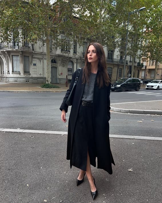 Elegant monochrome outfit with a black coat and pointed heels on a city street. 