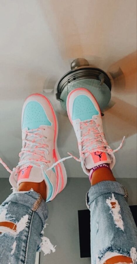 A pair of pastel pink and aqua blue Air Jordan 1 Mid GS 'Digital Pink' sneakers worn with distressed jeans, perfect for coffee outings.