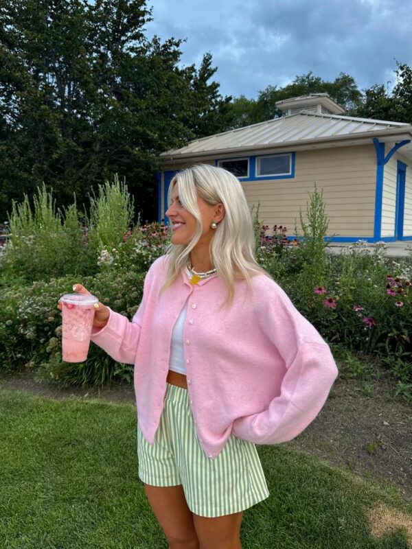 Woman wearing a pink cardigan, white crop top, and green striped shorts holding a pink drink