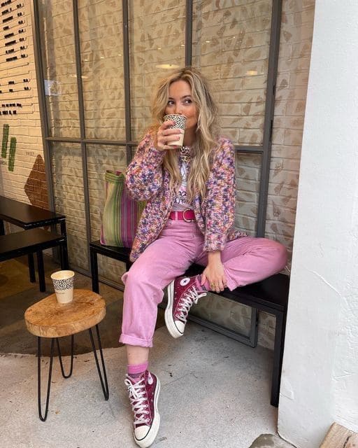 Woman wearing a multicolored knit jacket, pink pants, graphic tee, and red Converse sneakers
