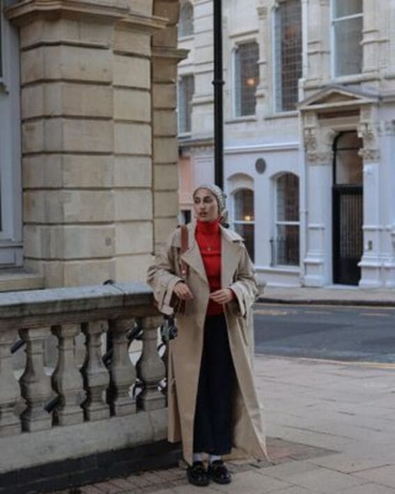 Trench coat styled with maxi skirt and red sweater to create a chic, layered style.