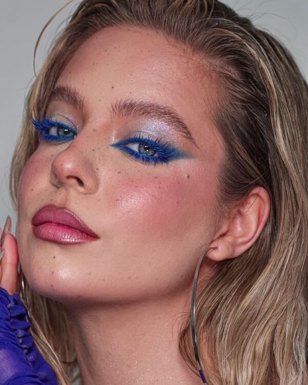 Close-up of a woman with electric blue cat eye makeup and glossy skin.