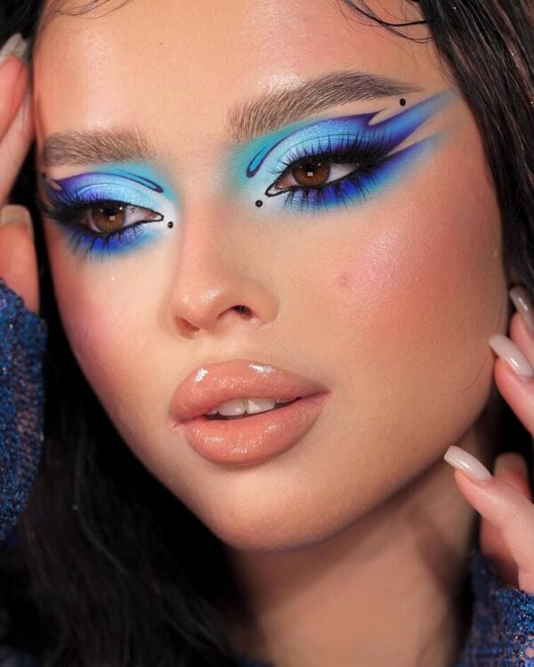 Model with blue graphic eye makeup and detailed swirl patterns around the eyes.