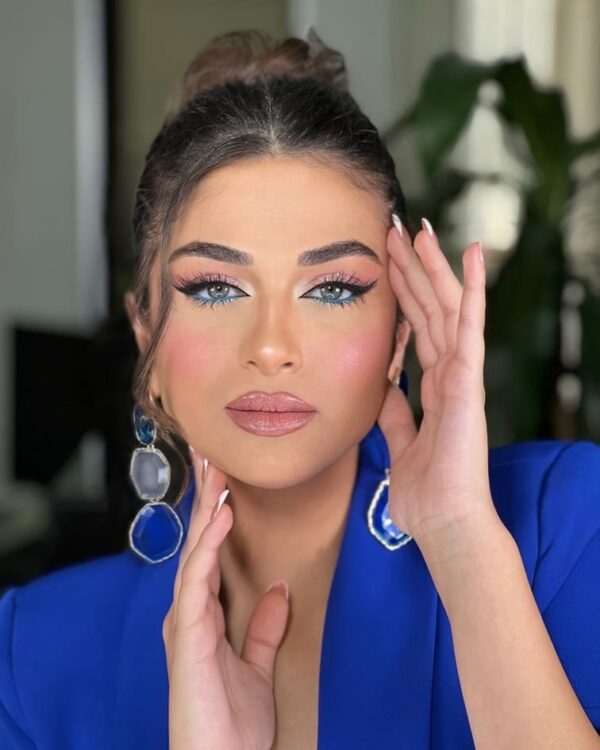 Woman with soft pastel blue eyeshadow in a subtle wing shape, paired with delicate makeup and glossy lips.