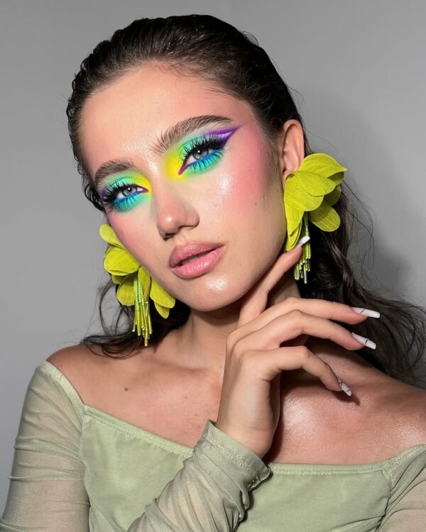 Women with vibrant neon blue and yellow eye makeup, pink blush, and subtle lips.