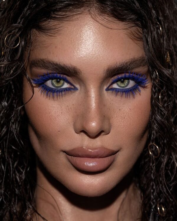 Woman with striking electric blue mascara on both upper and lower lashes.