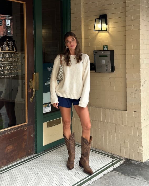 Effortless city look with a cozy sweater, shorts, and cowboy boots. 