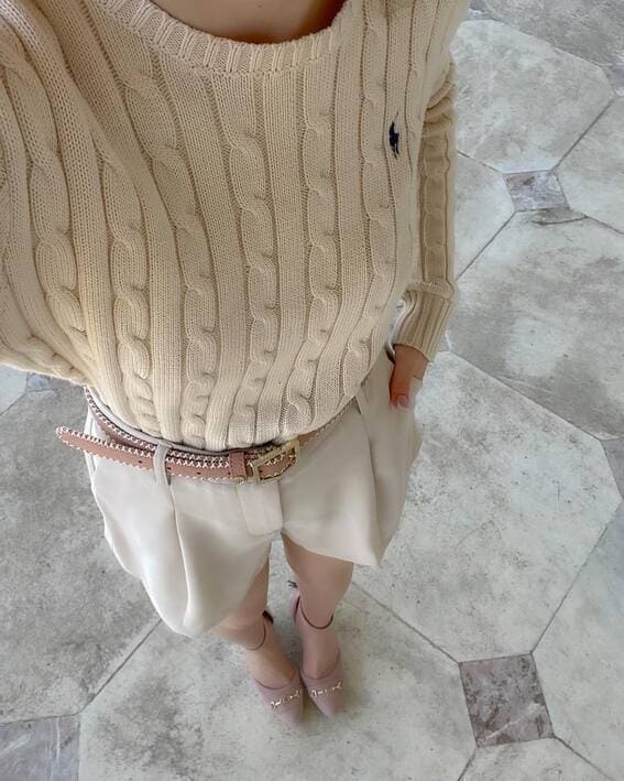 A woman wearing a cream cable knit sweater, tailored shorts, and blush pink loafers was photographed from above. 