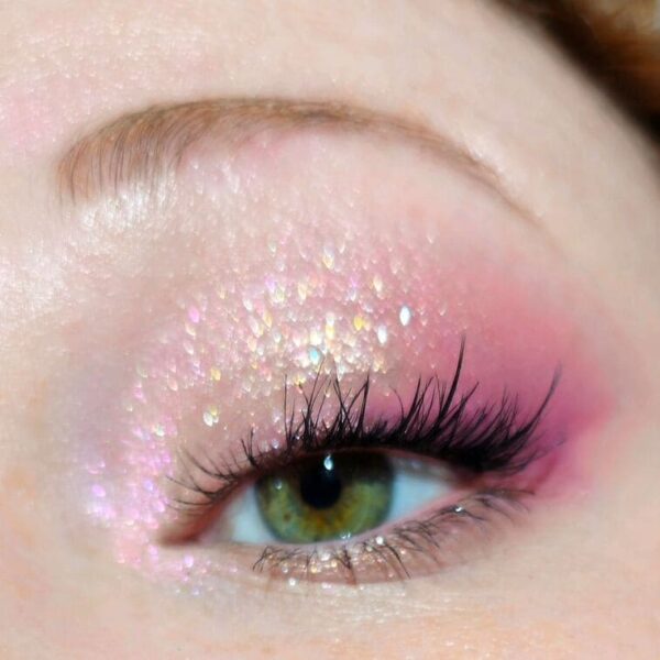 Close-up of iridescent, glittery pink eyeshadow on the eyelid with natural lashes.