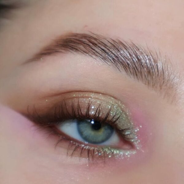 Close-up of subtle green and pink glitter eyeshadow with natural lashes.