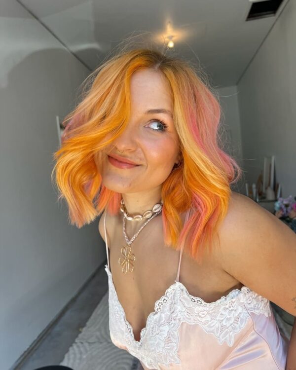 Side view of pink and peachy orange hair, highlighted in pastel shades.