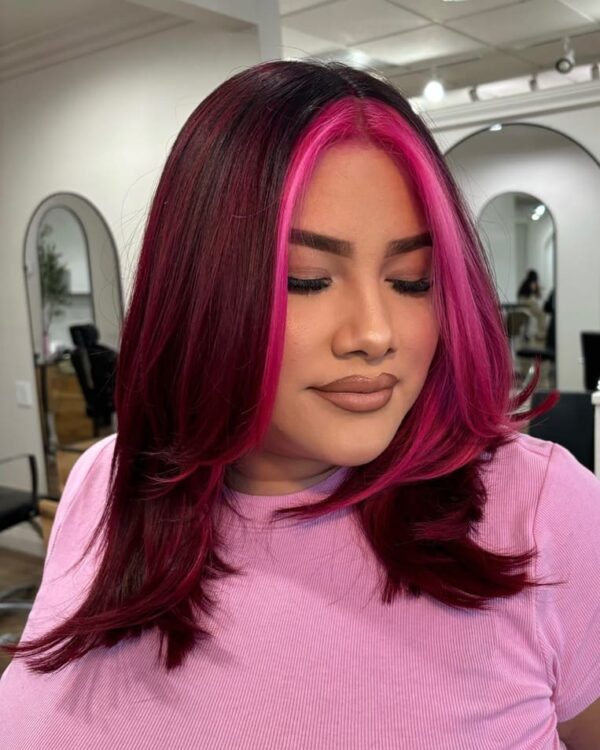 This is a frontal view of dark hair, with the vibrant color of a magenta-colored money piece framing the face.