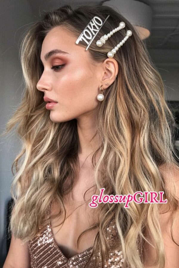 Long loose waves styled with statement pearl hair clips for a glam festival look.