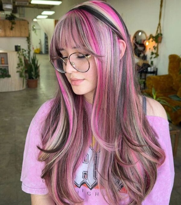 Pink and blonde highlighted hairstyle with bangs and soft waves.