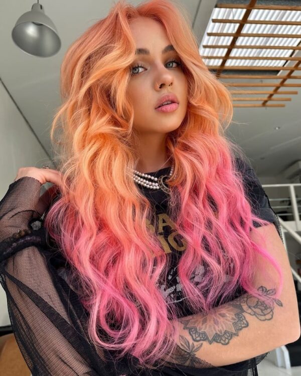 Wavy hair with a peach and neon pink gradient, styled with loose, voluminous curls.