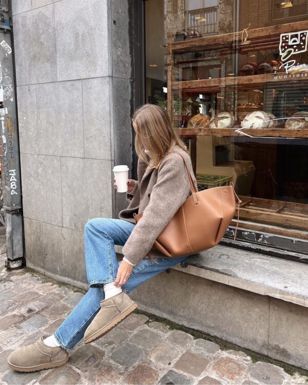 Casual fall look with a beige coat, blue jeans, and neutral UGGs.