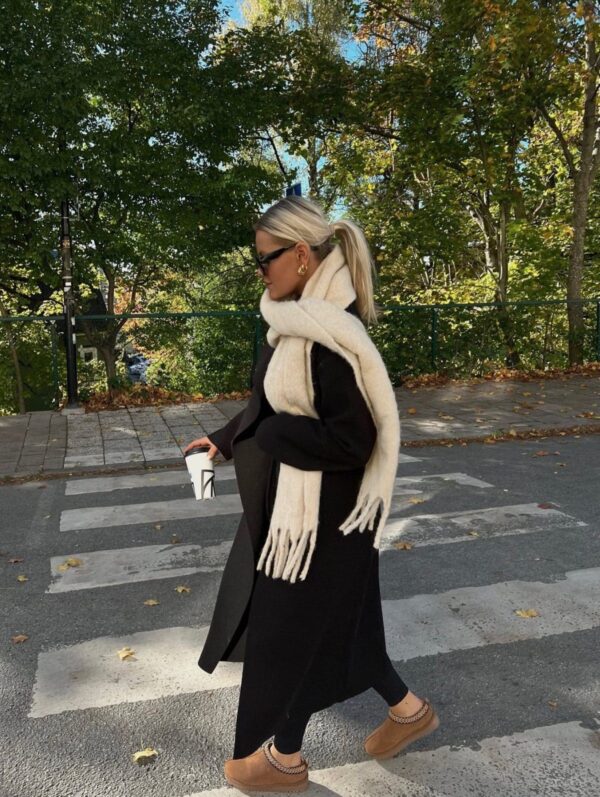 Warm winter outfit with a black coat, white scarf, and UGG Tasman slippers.