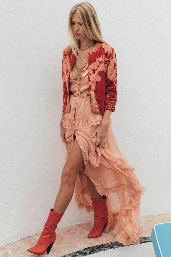 Woman wearing a peach ruffled maxi dress, embroidered red jacket, and red heeled boots