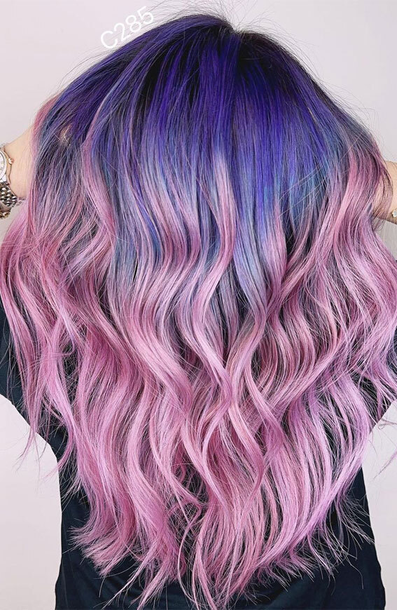 A long wavy hairstyle featuring a vivid dip dye blend from deep purple roots to bright pastel pink ends.
