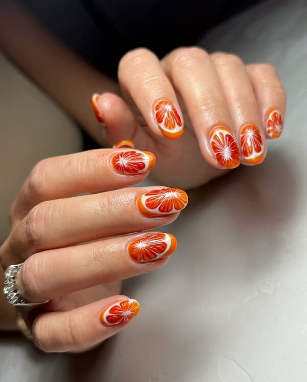 Vibrant orange and white floral burst nail design on almond-shaped nails for a playful, summer-ready vibe.