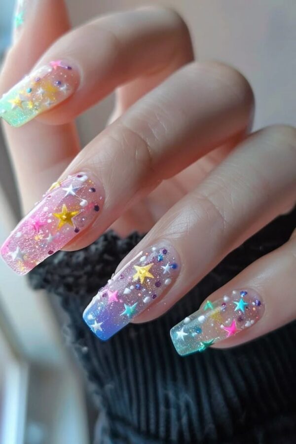 Close-up of long, coffin-shaped nails with a pastel ombre base decorated with tiny colorful stars, glitter, and gems.