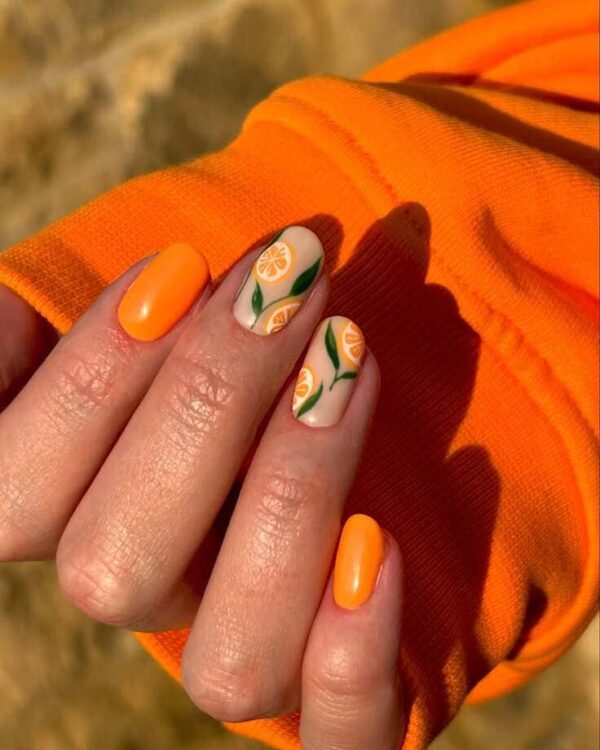 Juicy orange-themed nail design featuring bold orange polish and delicate fruit and leaf details over a creamy nude base.