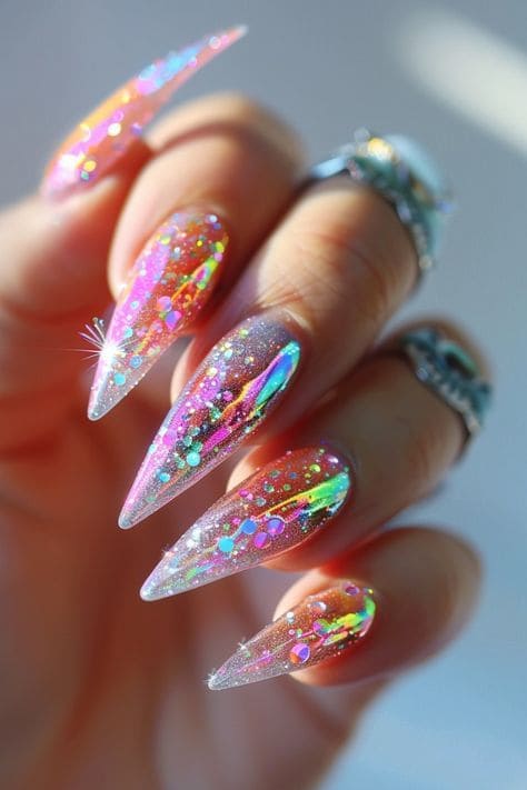 Hand with long, stiletto-shaped nails featuring holographic, glittery, multicolored summer nail art