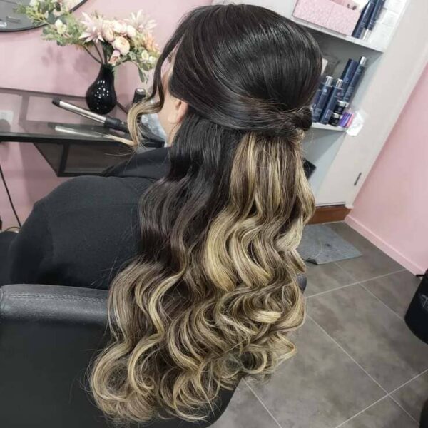 Long wavy hair with dark roots, blonde balayage, and a half-up twist