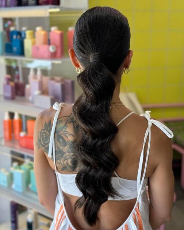 Sleek low ponytail with defined waves and wrapped hair tie