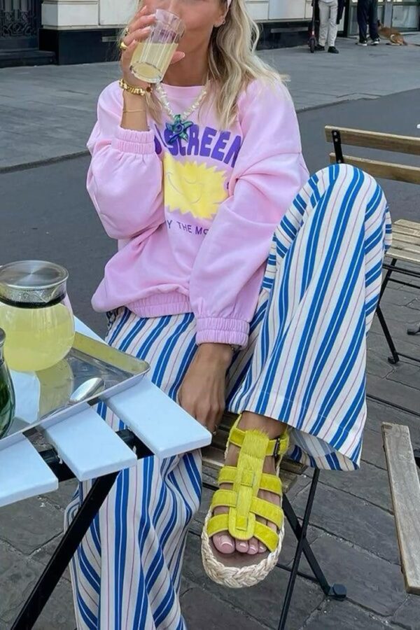 Woman wearing striped wide-leg pants, pink sweatshirt, and yellow sandals sitting at a café